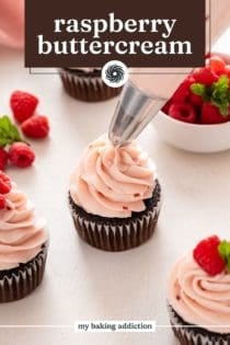 Piping bag piping raspberry frosting on top of a chocolate cupcake. Text overlay includes recipe name.