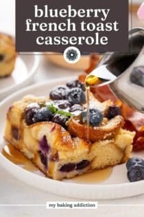 Syrup being poured over a slice of blueberry french toast casserole on a white plate. Text overlay includes recipe name.