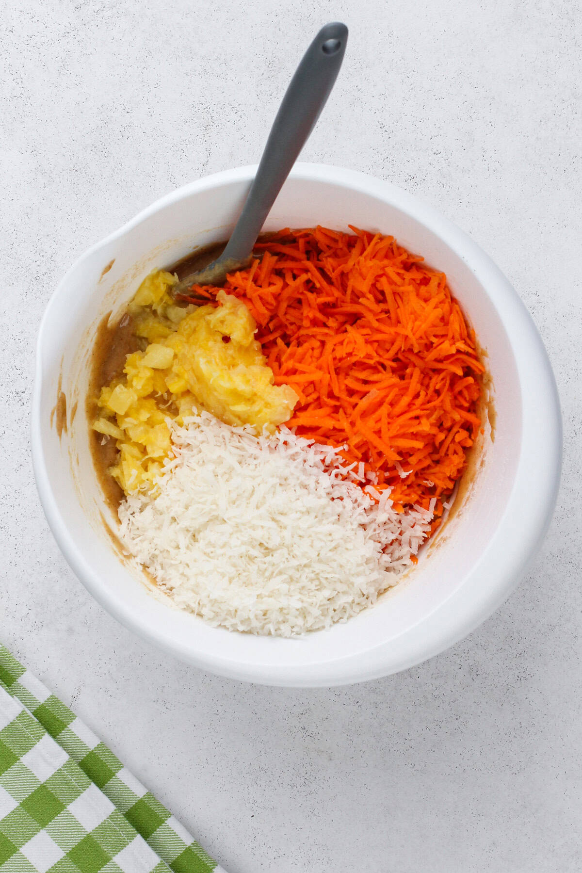 Shredded carrots, pineapple, and coconut being added to a bowl of batter for carrot cake bread.