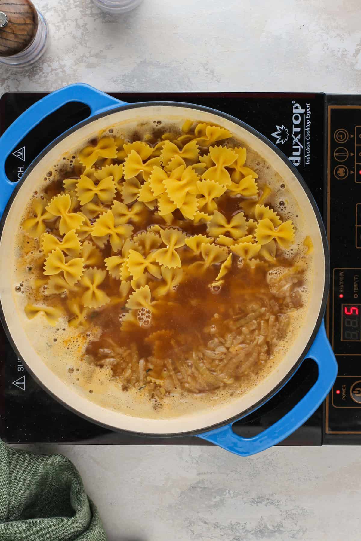 Pasta being added to simmering beef stock in a dutch oven.