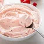 Raspberry buttercream frosting in a white bowl with a spoon.