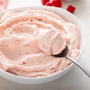 Raspberry buttercream frosting in a white bowl with a spoon.