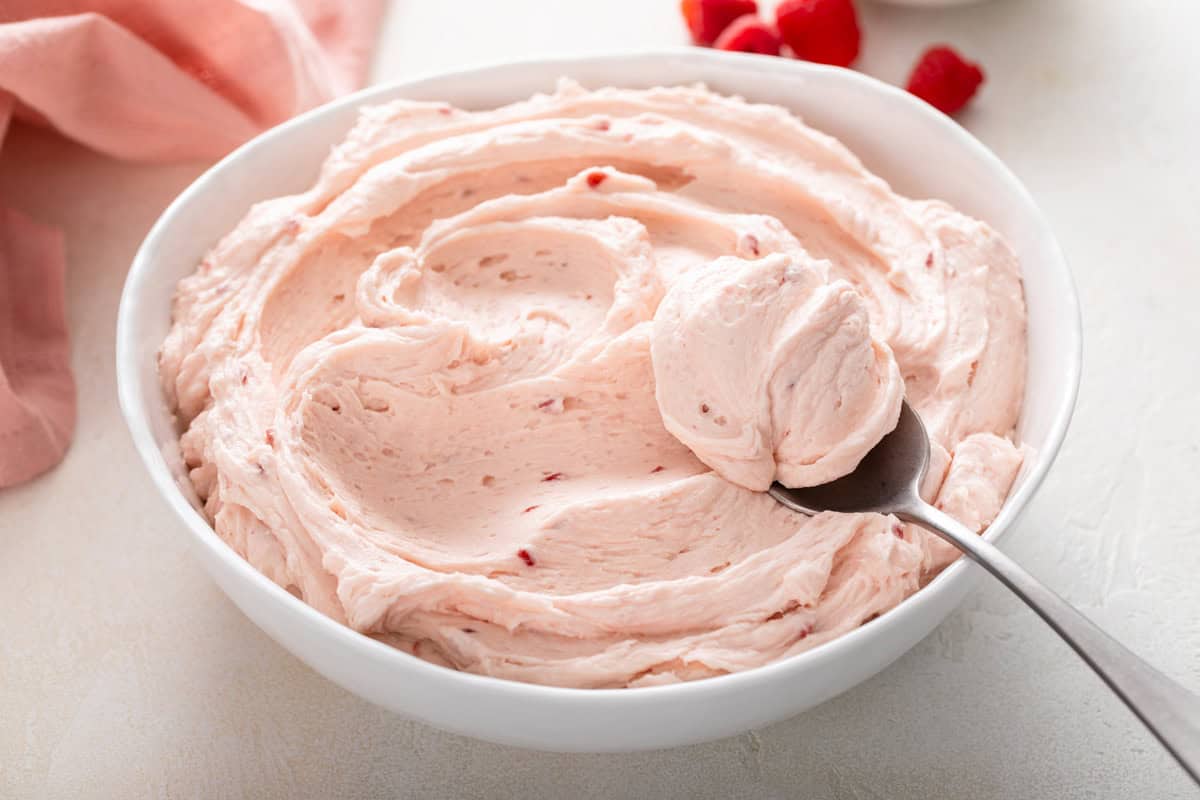 Spoon in a white bowl of raspberry buttercream frosting.
