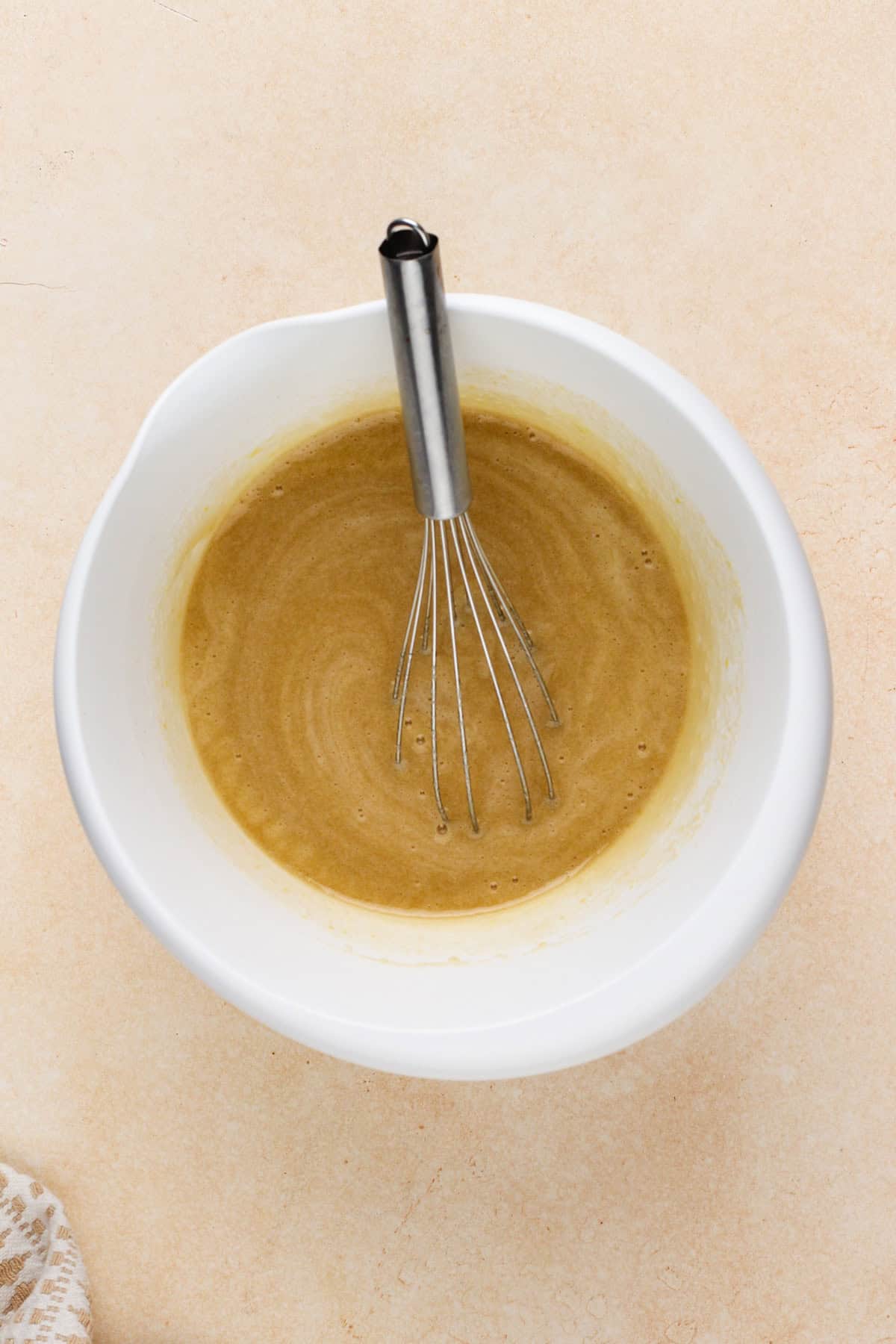 Wet ingredients for carrot cake bars whisked in a white bowl.