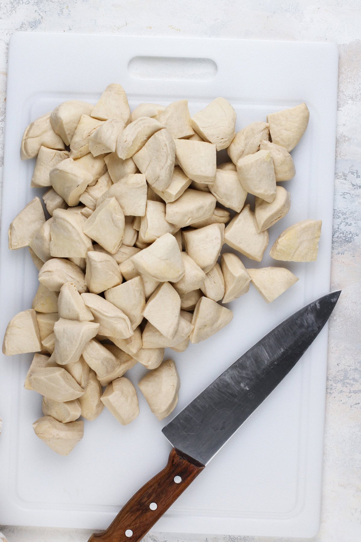 Canned biscuits cut into quarters on a white cutting board.
