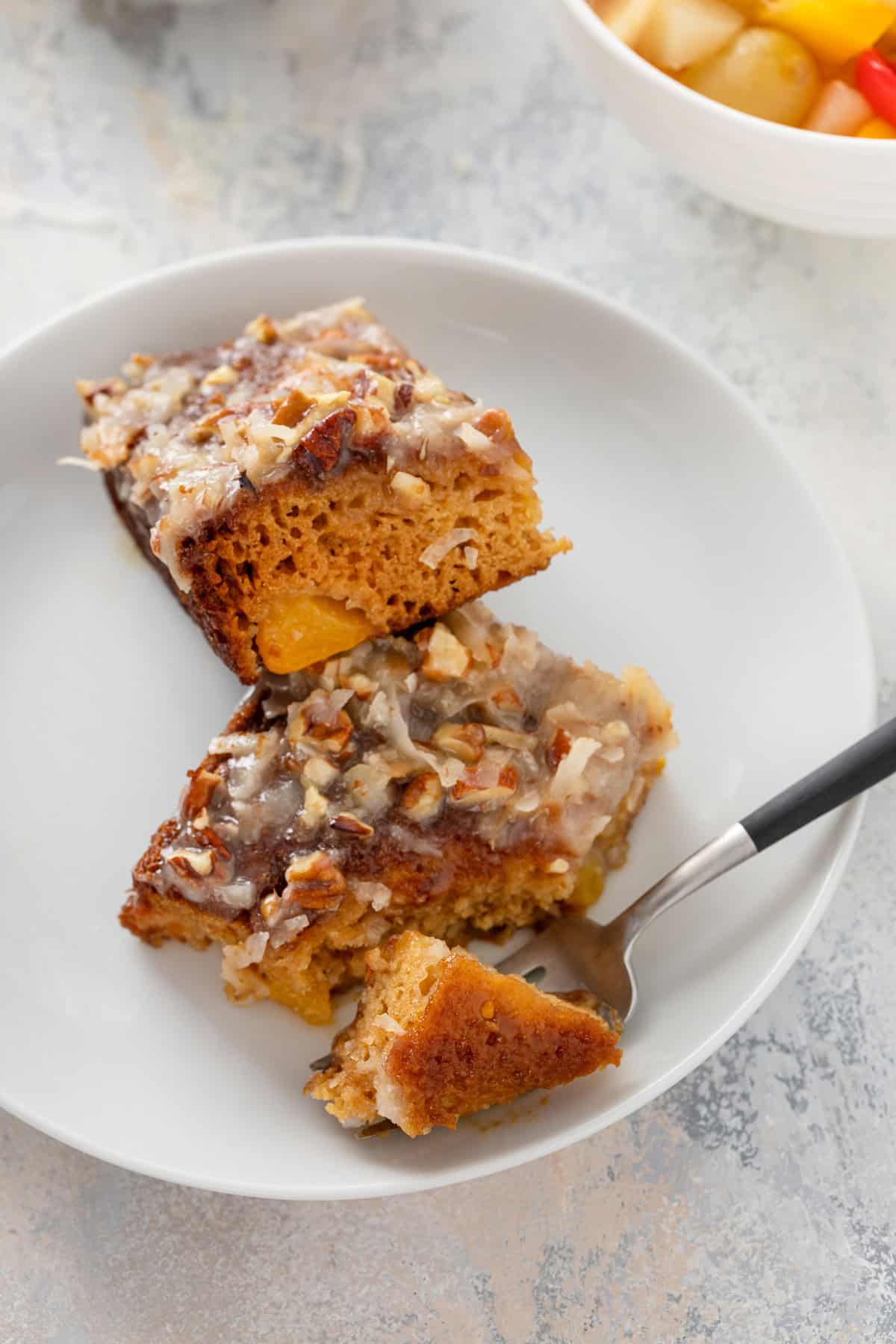 Fork cutting a corner from a slice of fruit cocktail cake on a white plate.