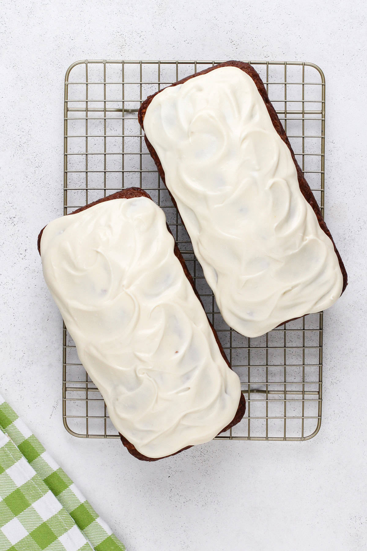 Two loaves of carrot cake bread topped with cream cheese glaze on a wire rack.