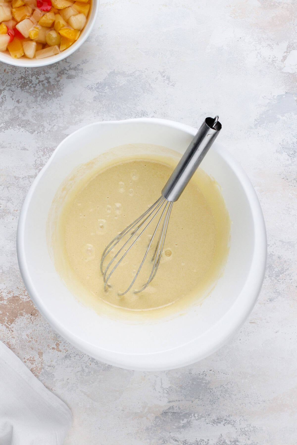 Wet ingredients for fruit cocktail cake whisked in a white bowl.
