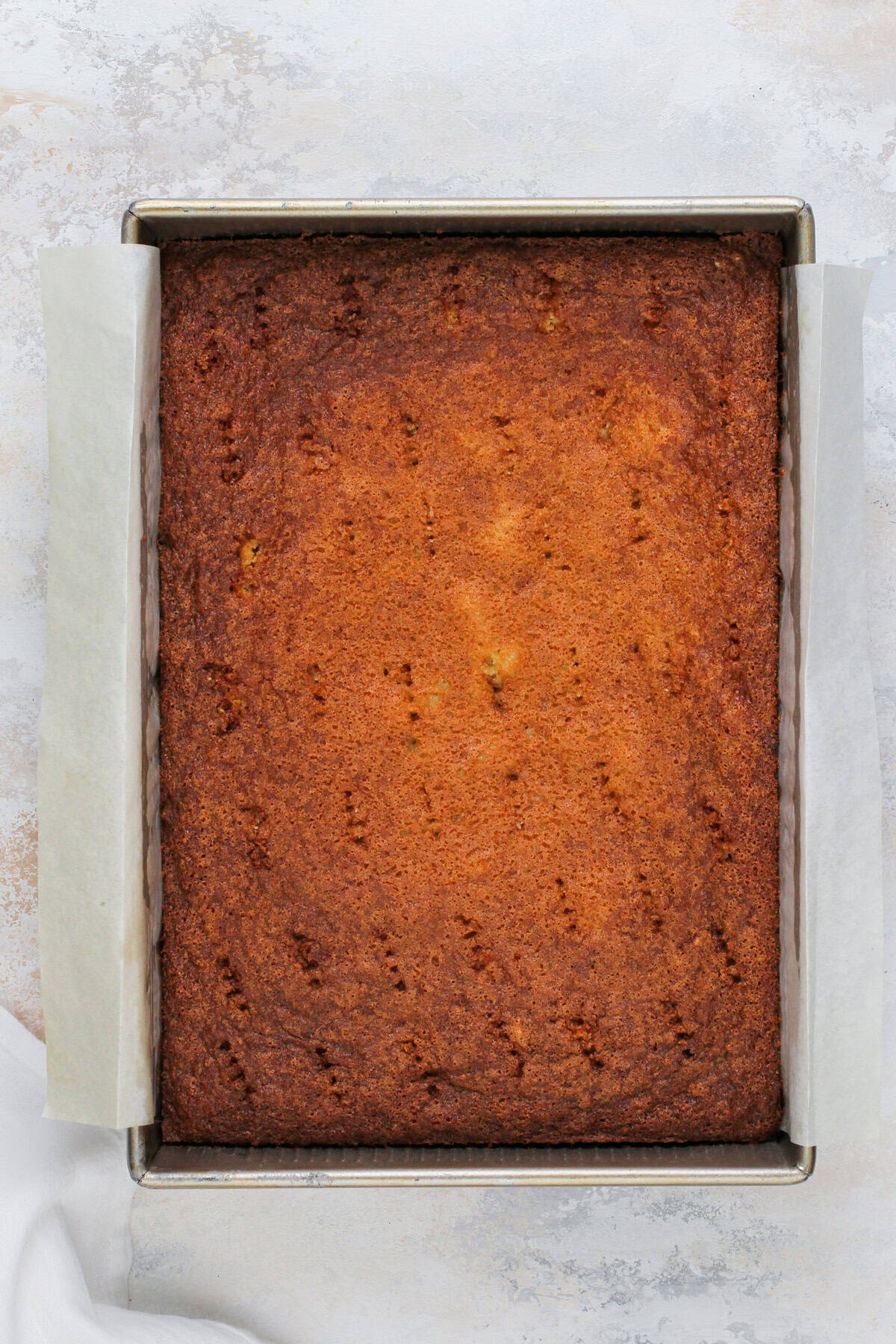 Baked fruit cocktail cake with holes poked across the top with a fork.