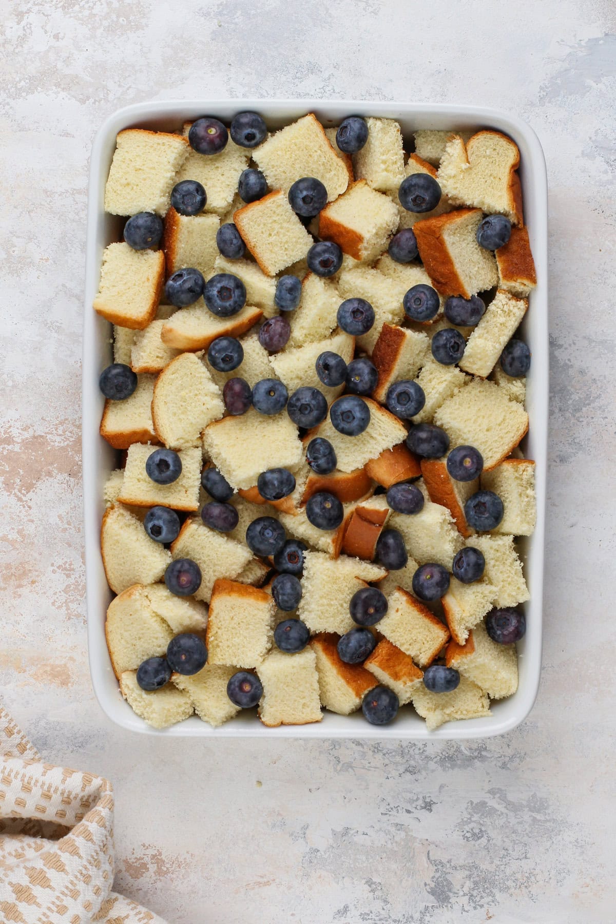 Cubes of brioche and blueberries arranged in a white baking dish.