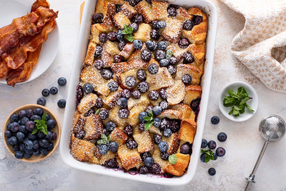 Overhead view of blueberry french toast casserole, dusted with powdered sugar in a white baking dish.