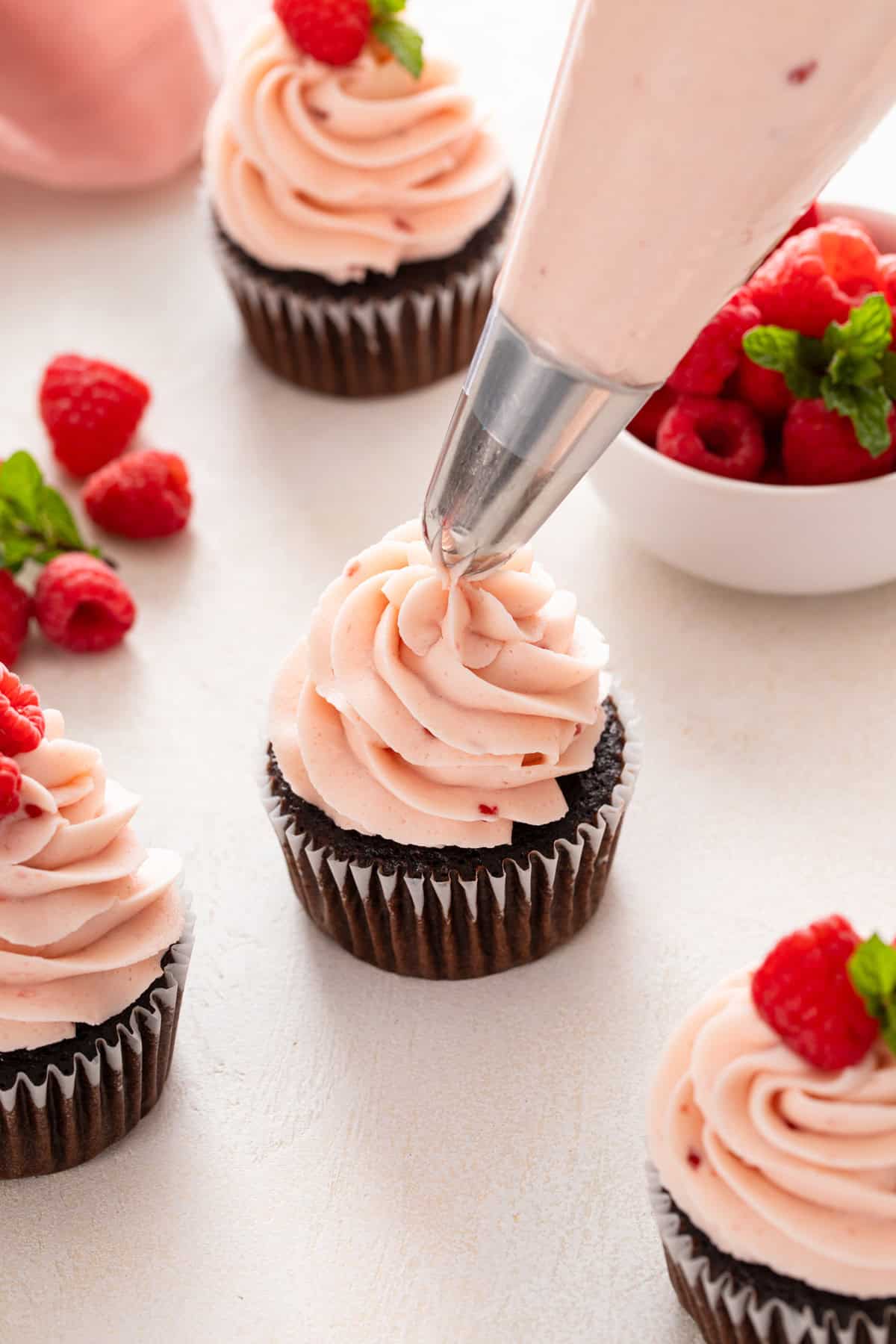 Piping bag piping raspberry frosting on top of a chocolate cupcake.