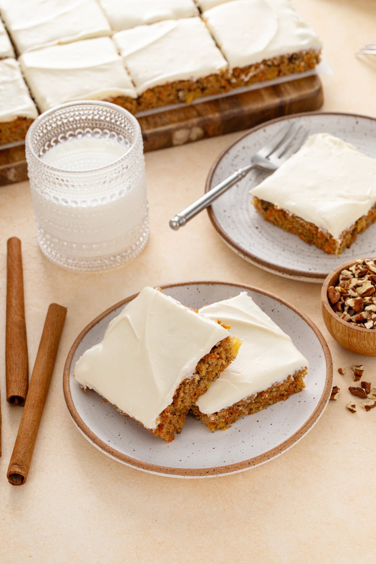 Plated carrot cake bars next to a glass of milk.