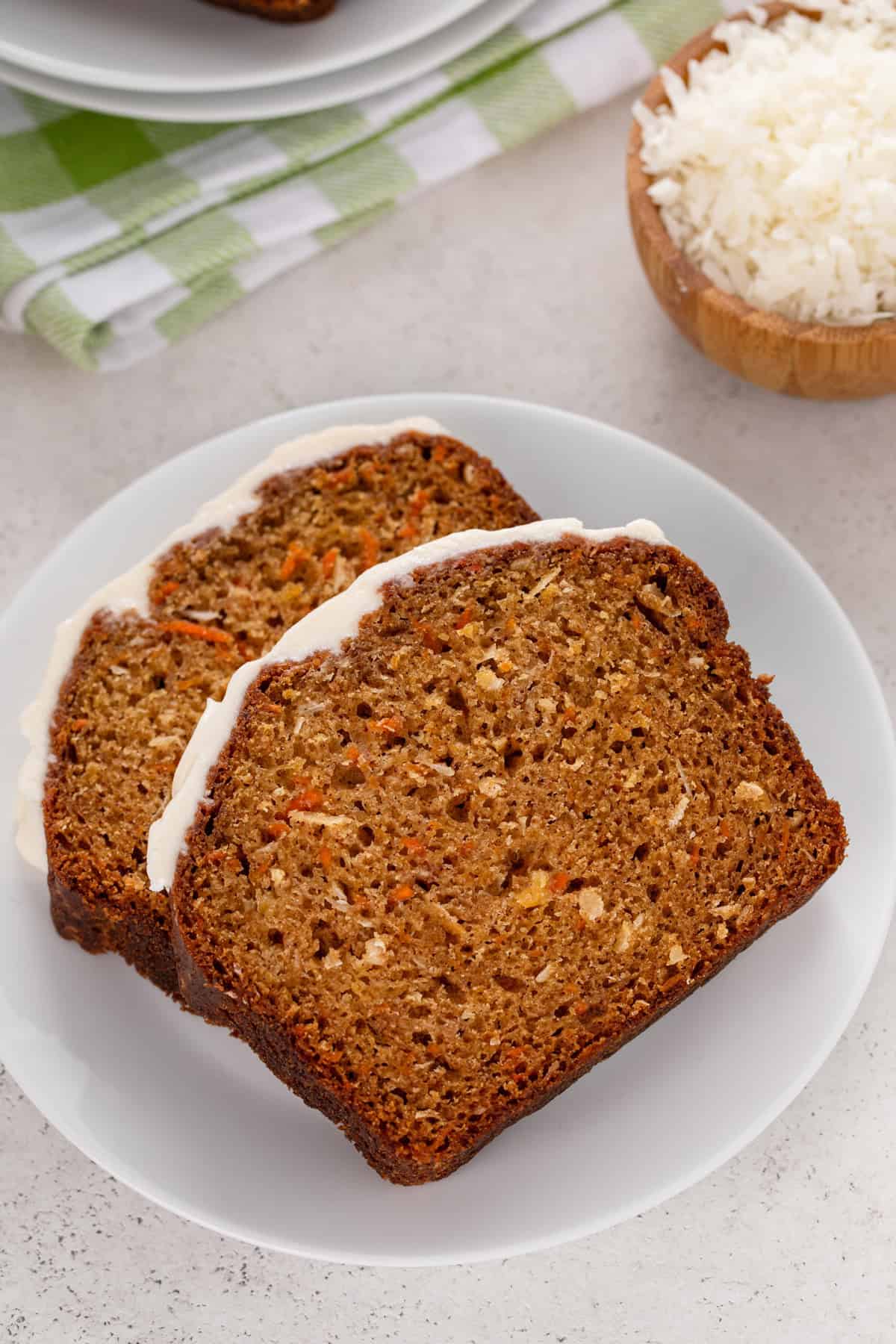 White plate holding two slices of carrot cake bread topped with cream cheese glaze.