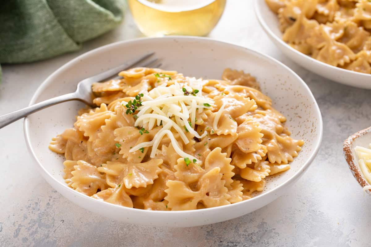 Fork in a white bowl filled with french onion pasta with a glass of white wine in the background.