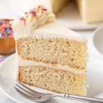 Slice of vanilla cake on a white plate next to a fork.