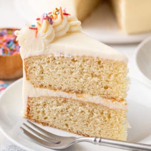 Slice of vanilla cake on a white plate next to a fork.
