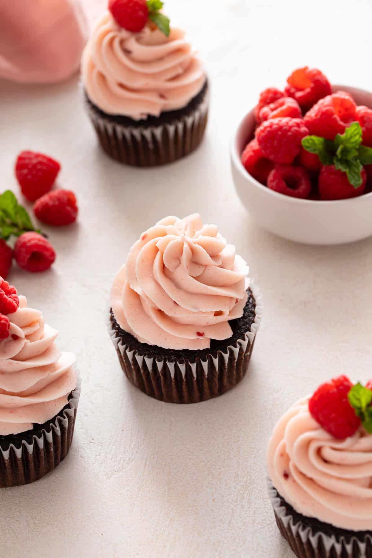 Chocolate cupcakes topped with raspberry buttercream arranged on a countertop.
