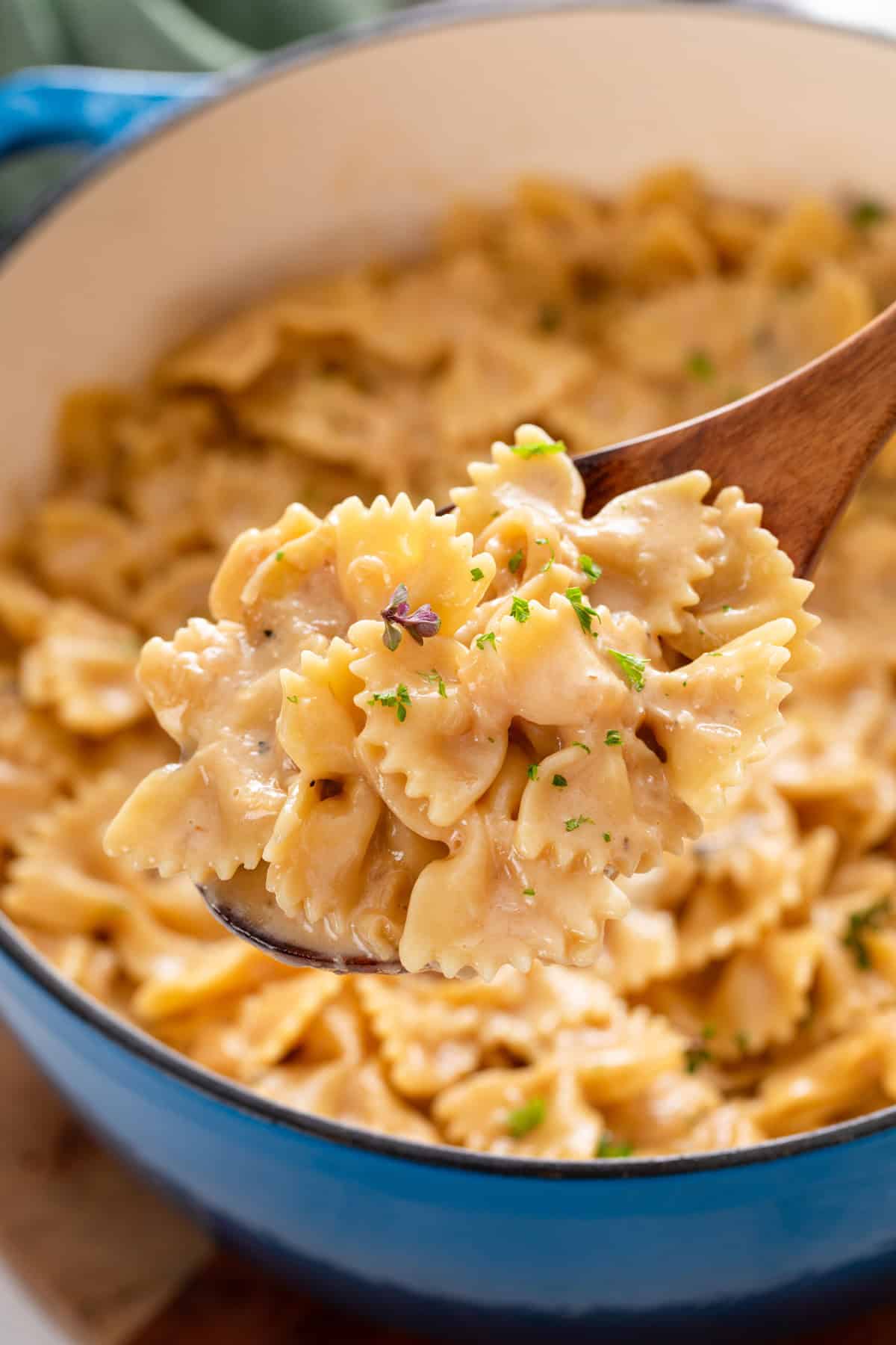 Spoon holding up a serving of french onion pasta over the pot.