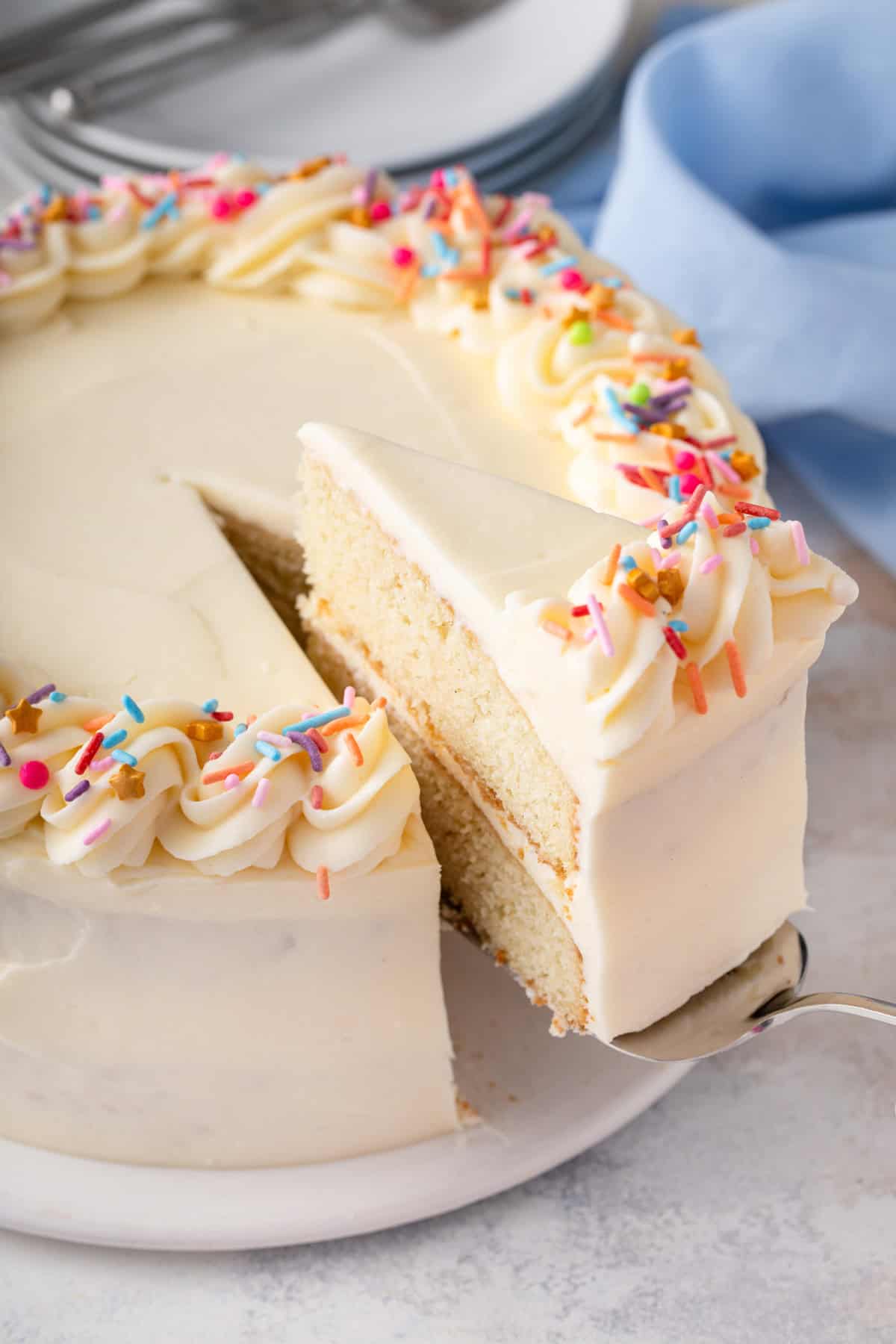 Cake server lifting up a slice of vanilla layer cake.