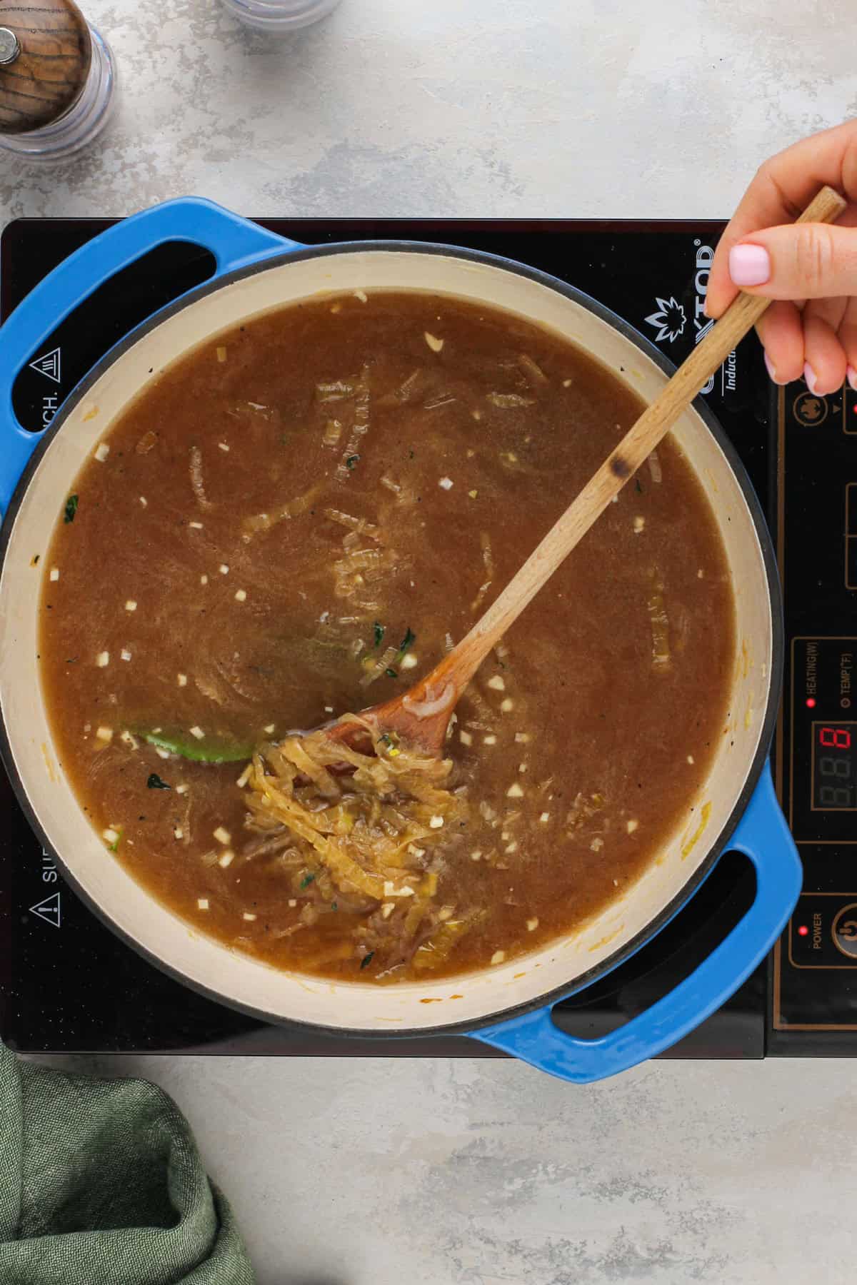 Beef stock, herbs, and caramelized onions being stirred together.