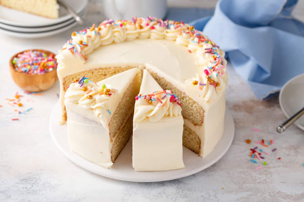 Sliced vanilla layer cake decorated with rainbow sprinkles.