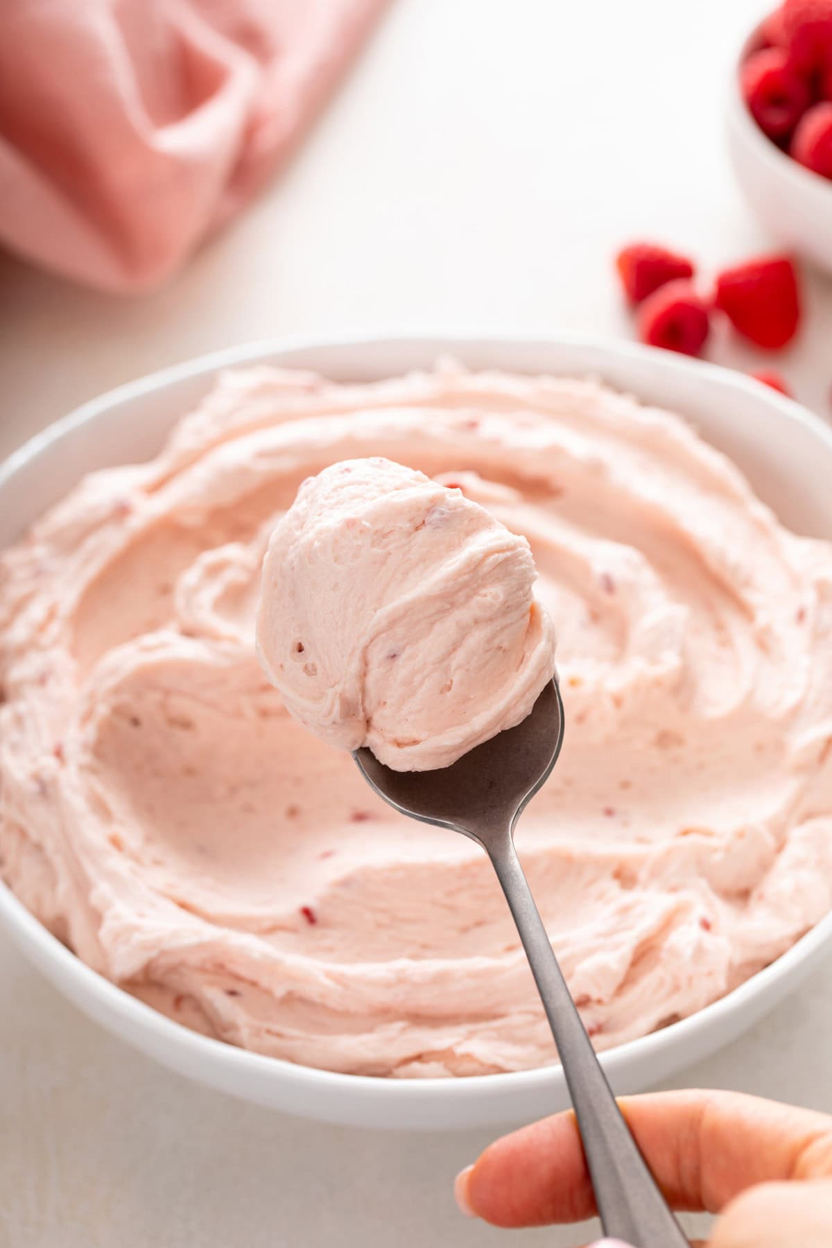 Spoon holding up a bite of raspberry buttercream frosting.