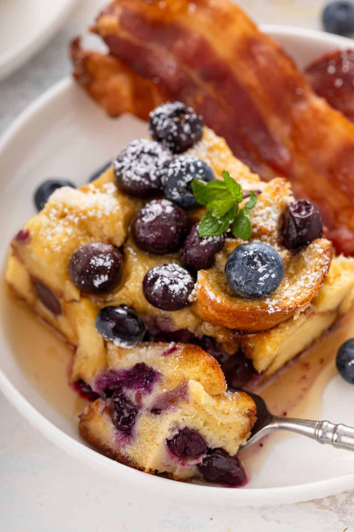 Fork cutting a bite from the corner of a slice of blueberry french toast casserole.