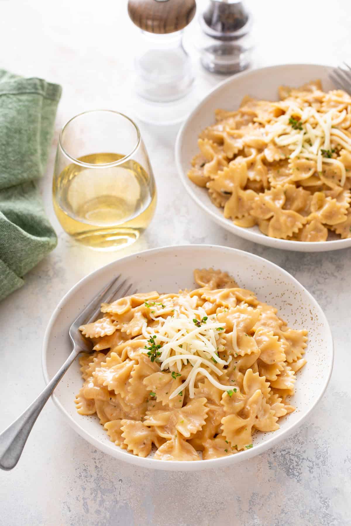 Two white pasta bowls filled with french onion pasta next to a glass of wine.