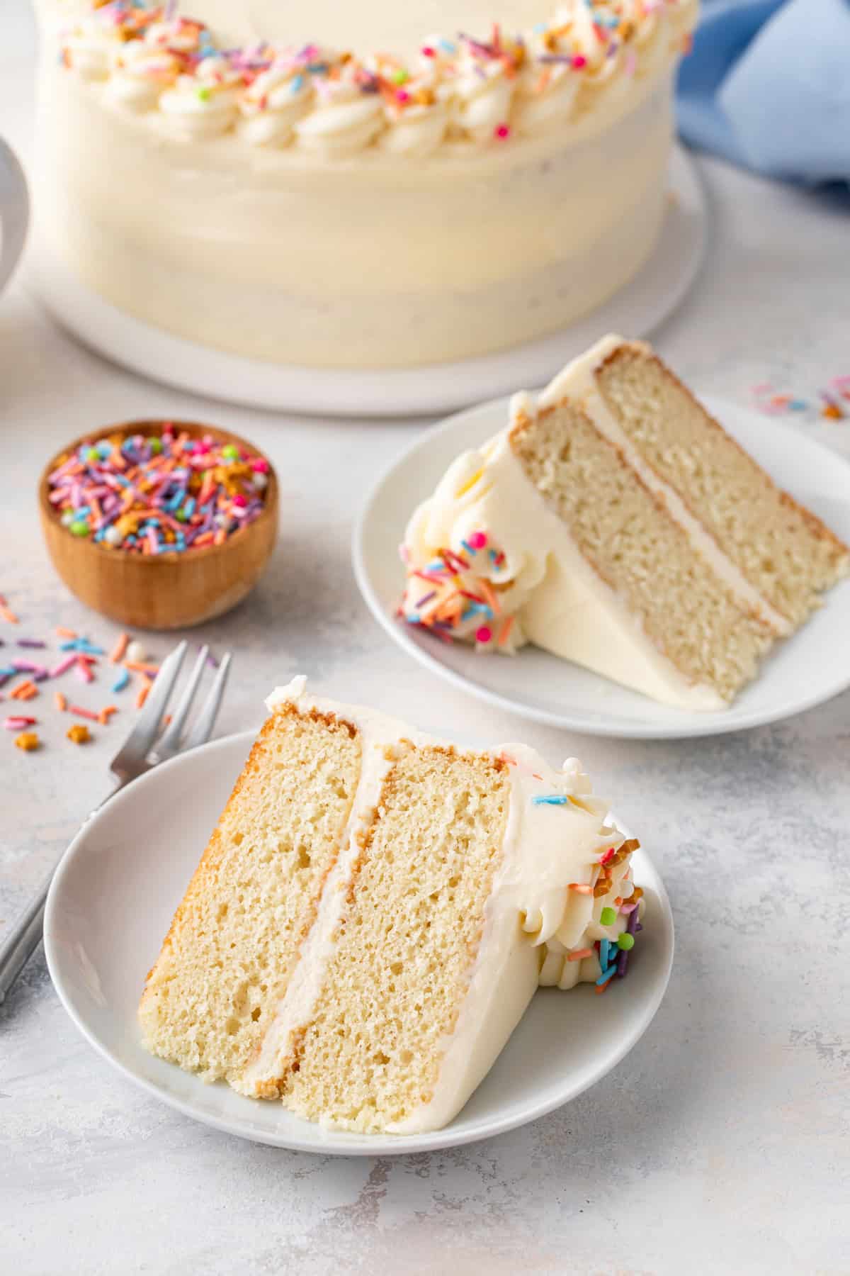 Two white plates, each holding a slice of vanilla layer cake.