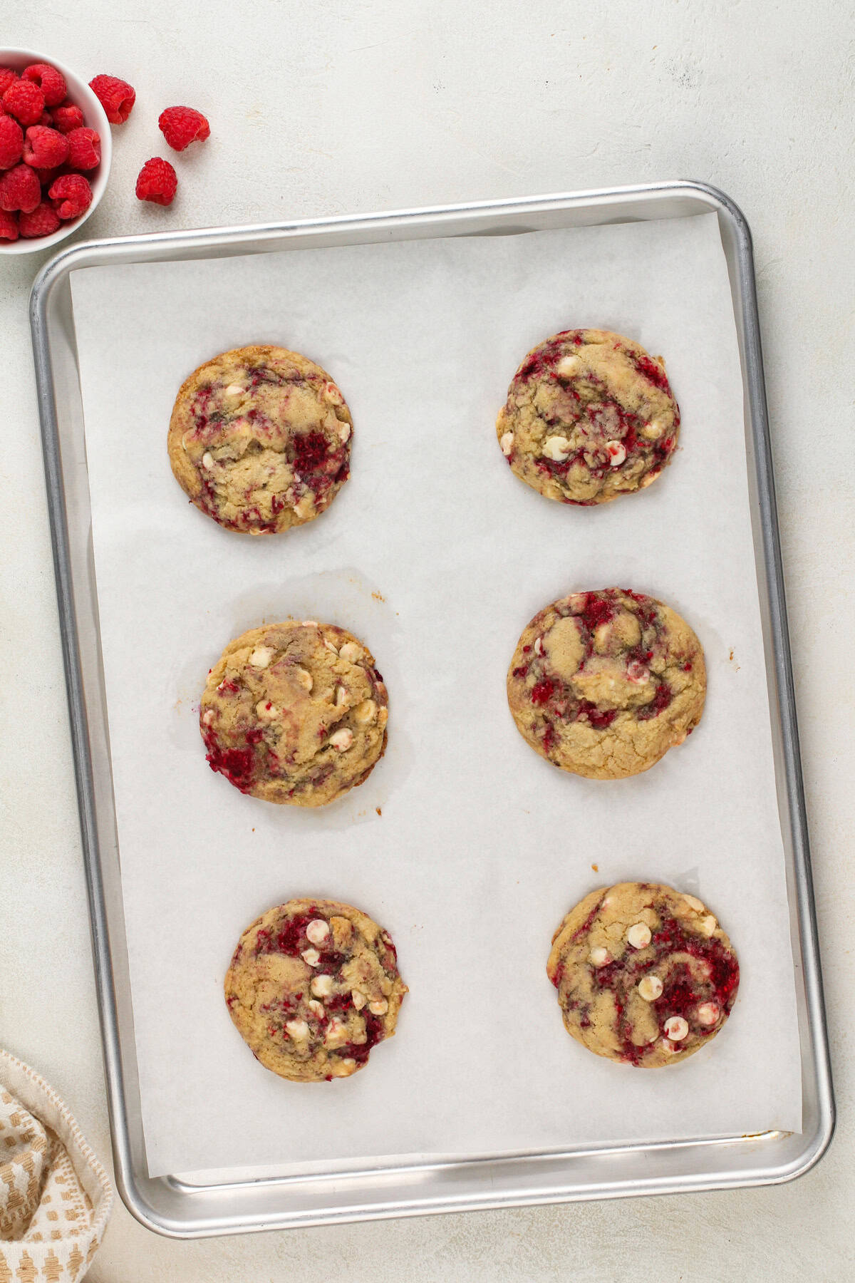 6 white chocolate raspberry cookies cooling on a parchment-lined baking sheet.
