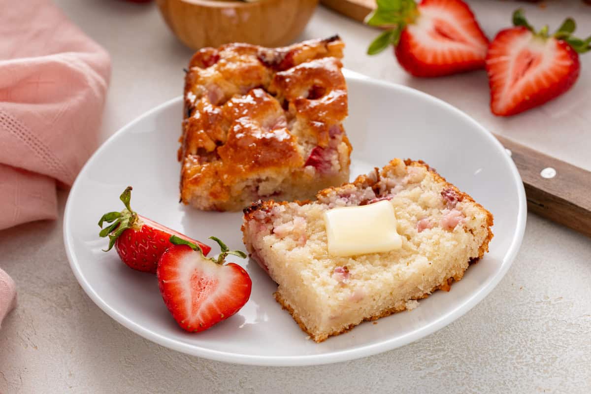 Halved strawberry biscuit topped with butter on a white plate.