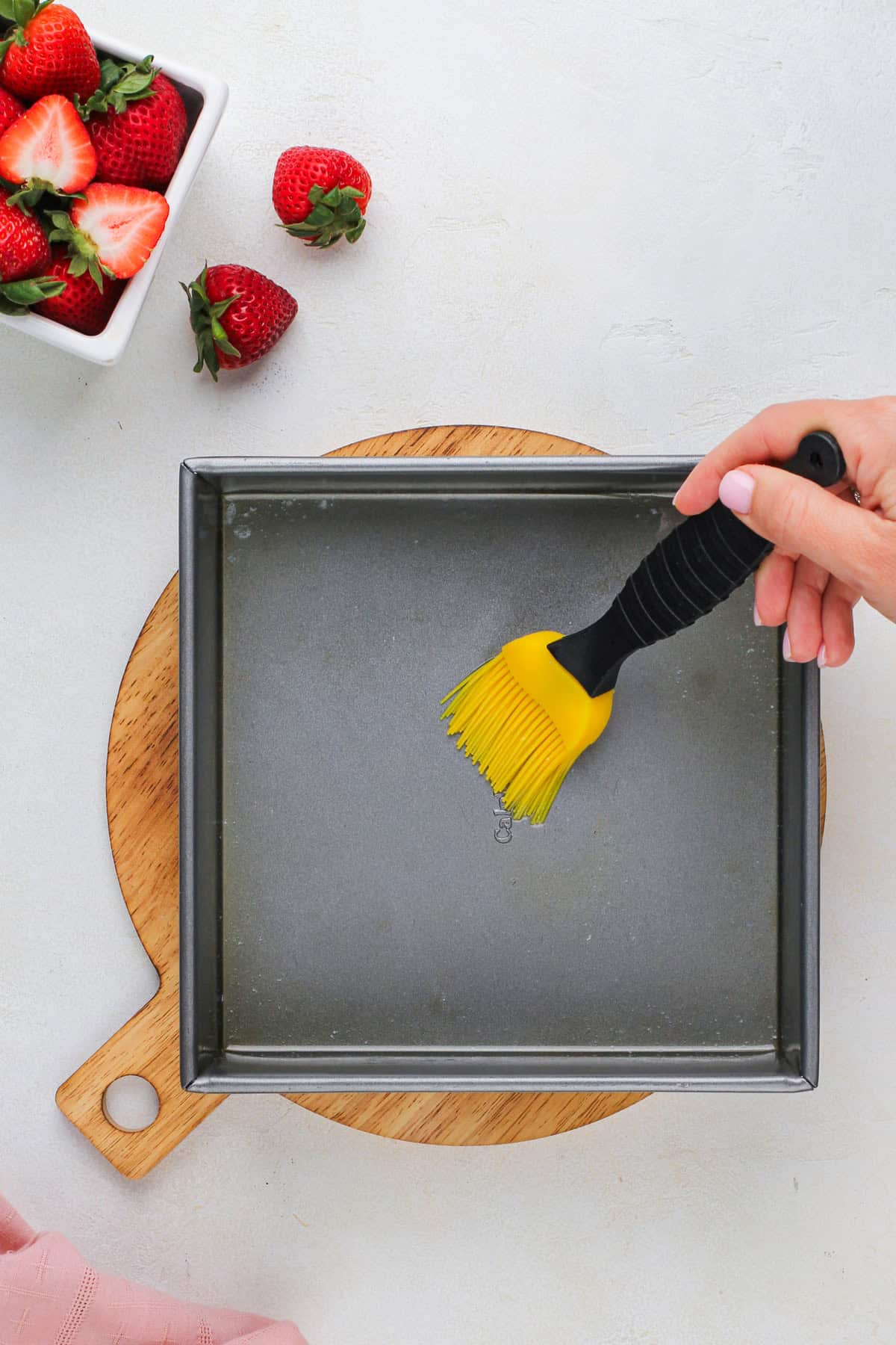 Melted butter being brushed across the bottom of a baking pan.