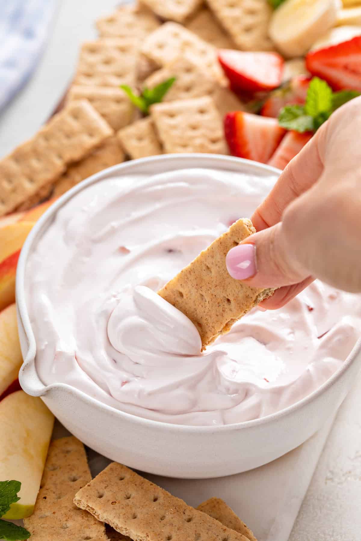 Hand dipping a graham cracker into yogurt fruit dip.