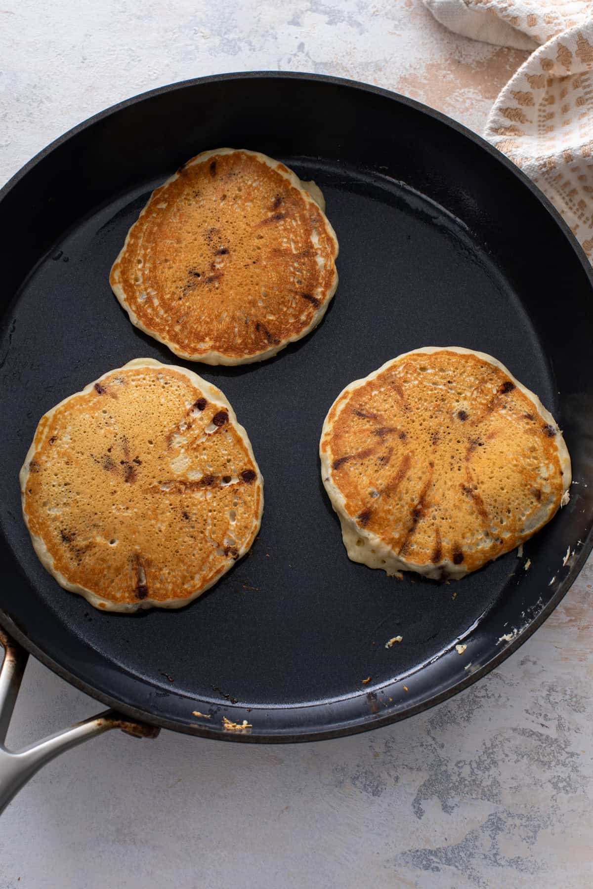 Three chocolate chip pancakes flipped in a skillet.