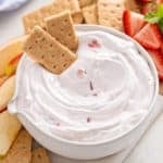 Bowl of yogurt fruit dip with two graham crackers in it.