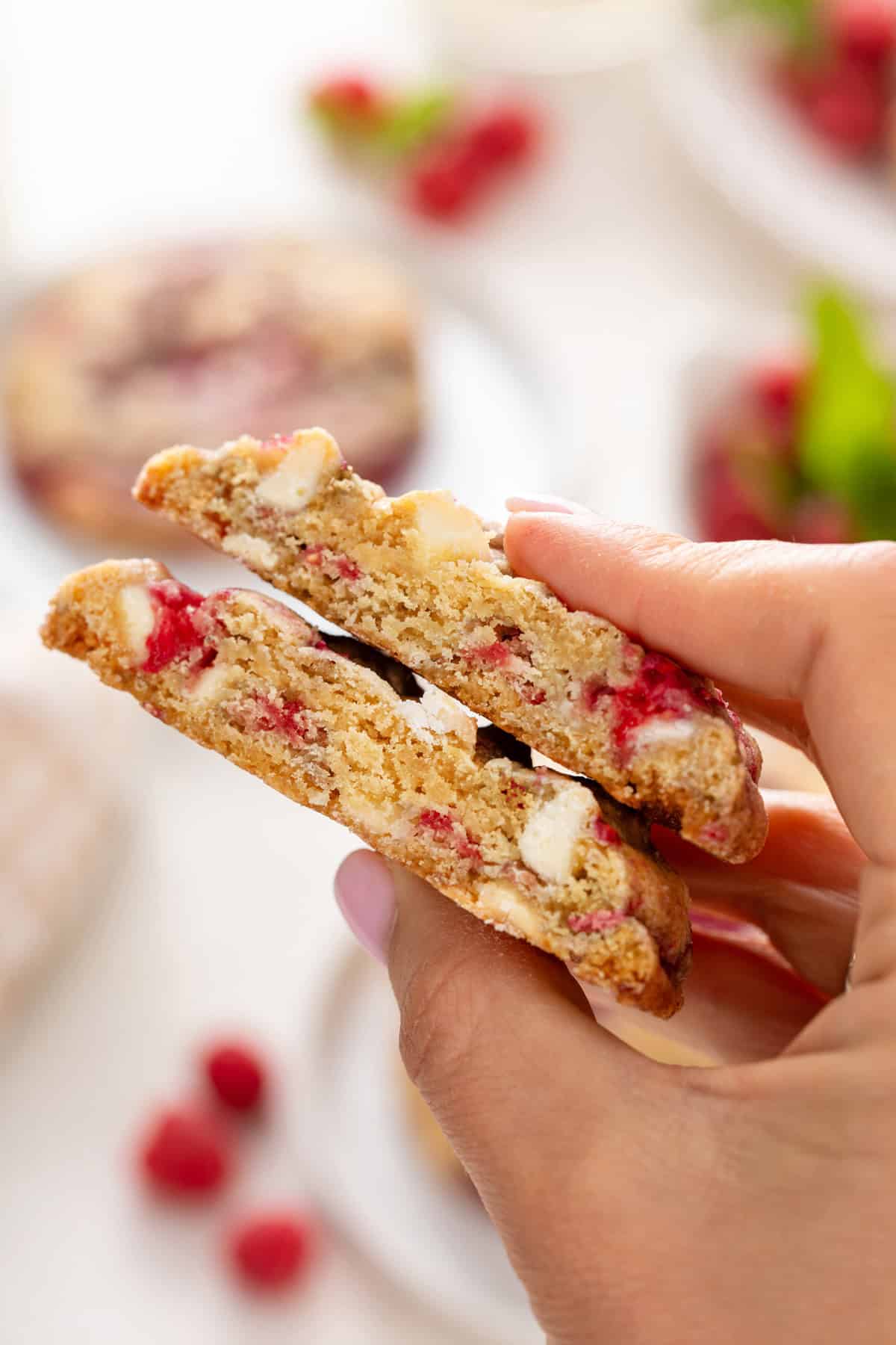 Hand holding up a halved white chocolate raspberry cookie.