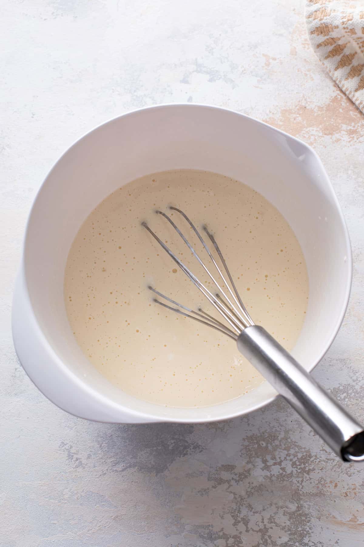 Wet ingredients for pancakes whisked in a white bowl.