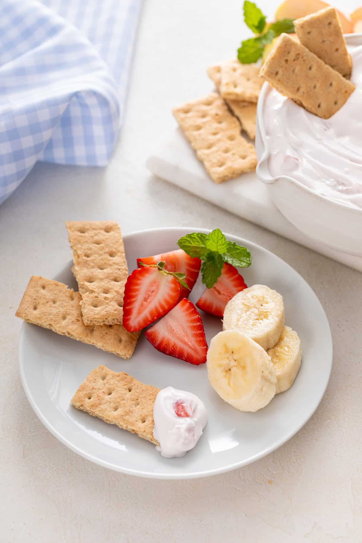 Yogurt fruit dip, graham crackers, fresh strawberries and banana slices on a white plate.