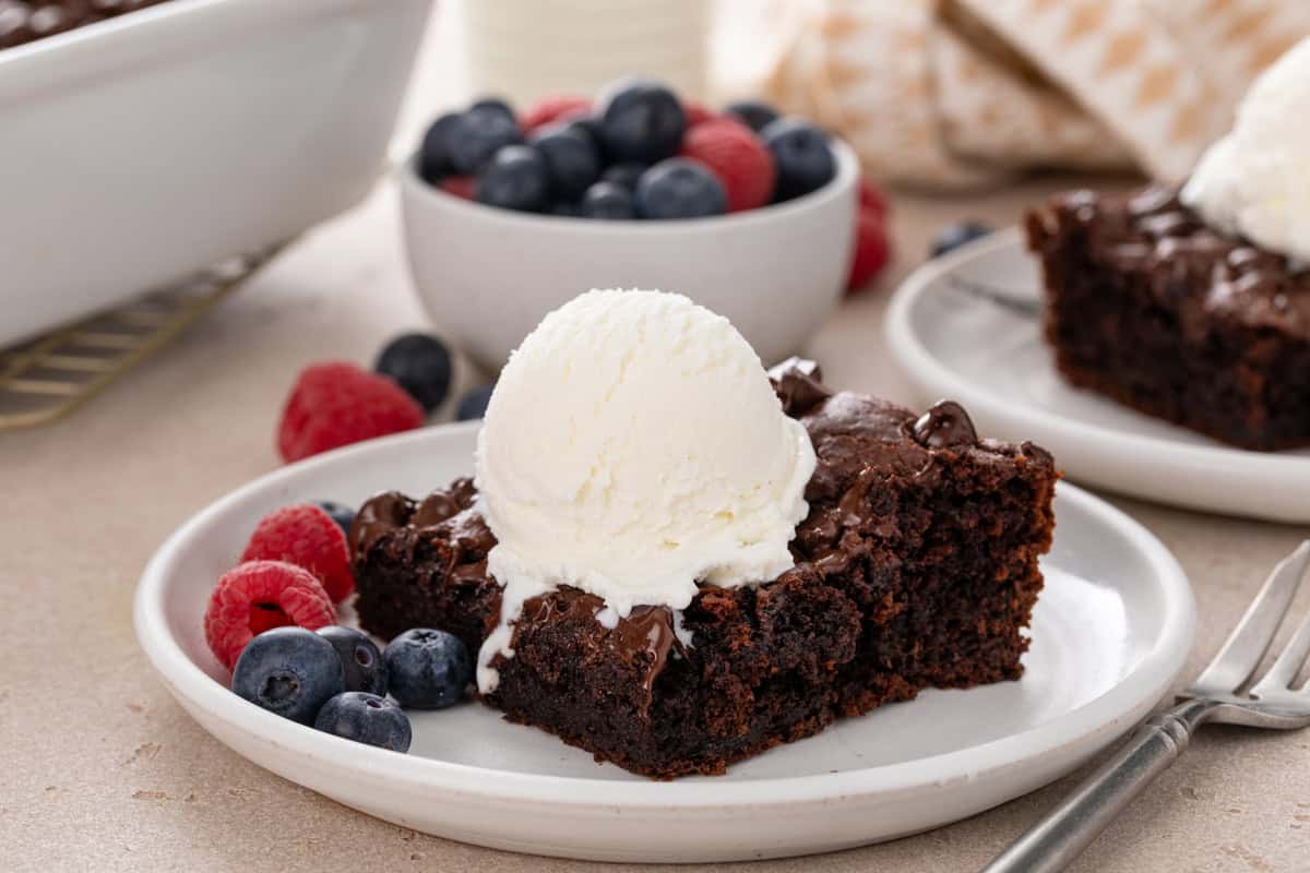 Slice of chocolate dump cake topped with a scoop of vanilla ice cream on a white plate.
