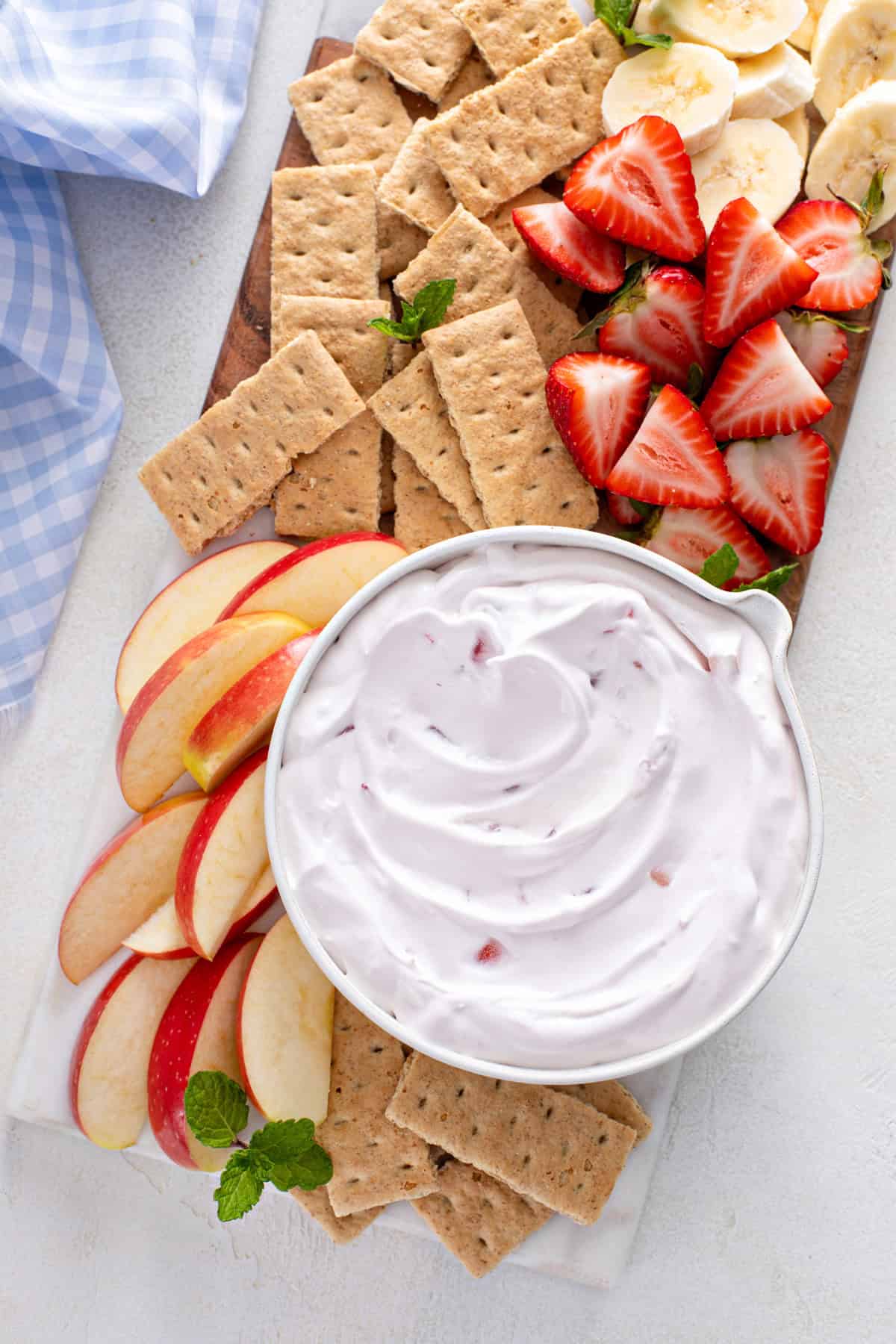 Overhead view of a bowl of yogurt fruit dip on a platter surrounded by graham crackers and fresh fruit.