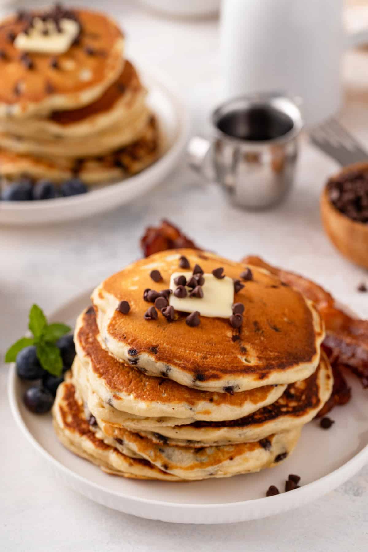 Stack of chocolate chip pancakes topped with a pat of butter on a white plate.