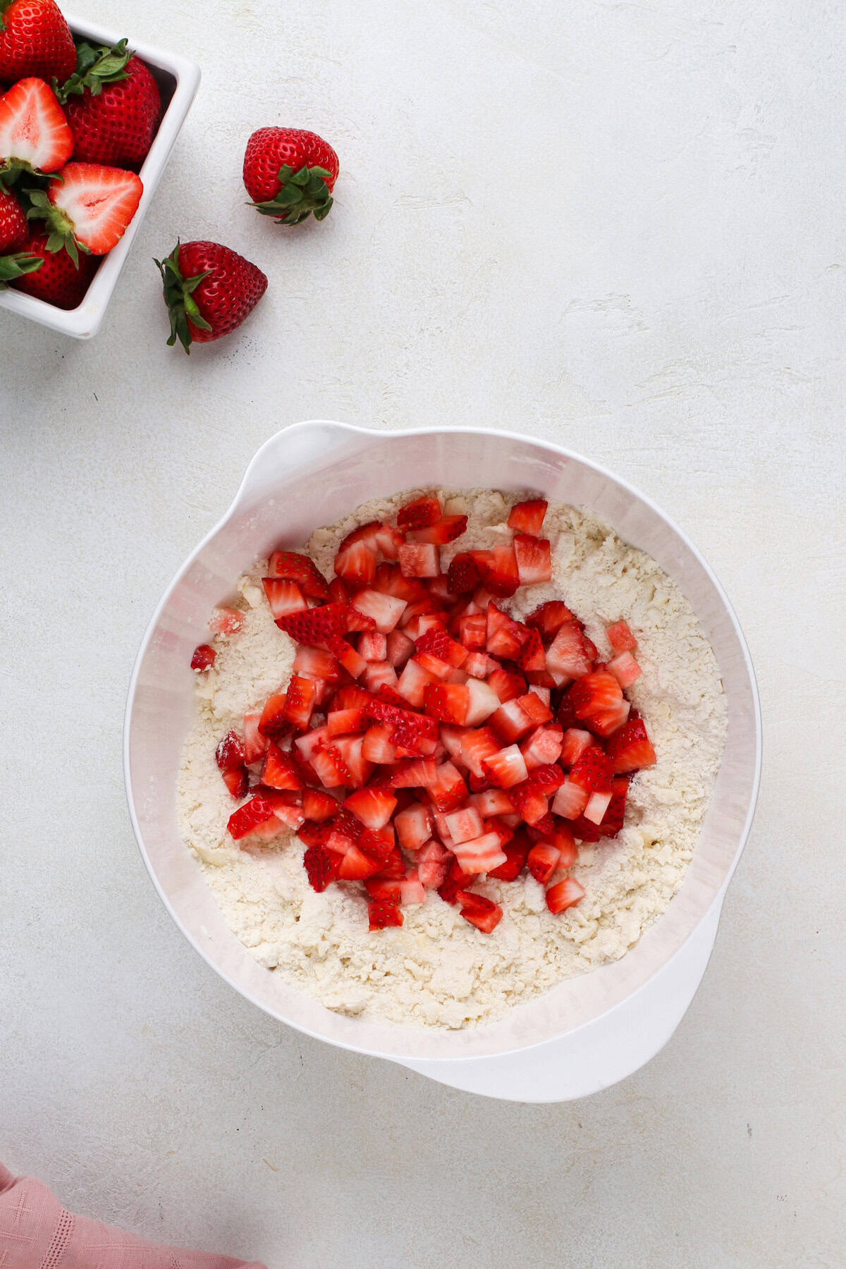 Diced strawberries added to a bowl of butter worked into flour.