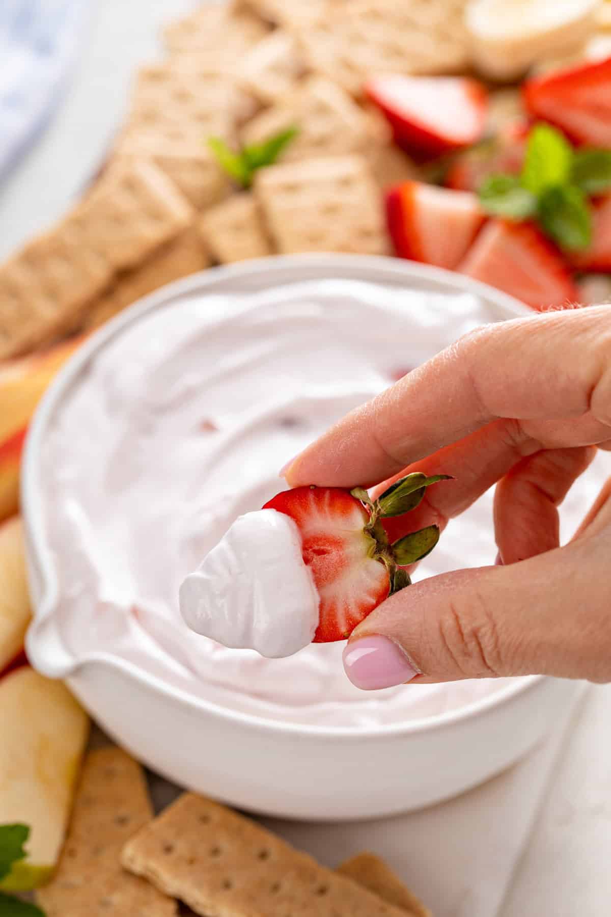 Hand holding up a halved fresh strawberry that's been dipped in yogurt fruit dip.