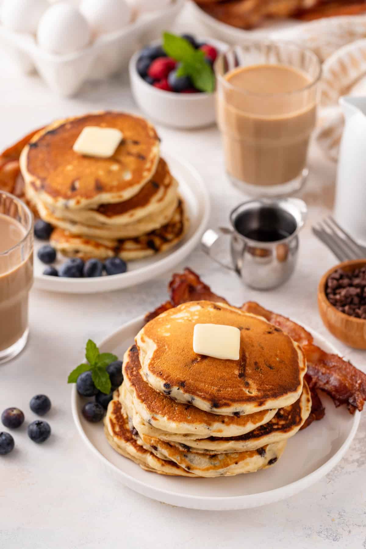 Two white plates filled with stacks of chocolate chip pancakes.