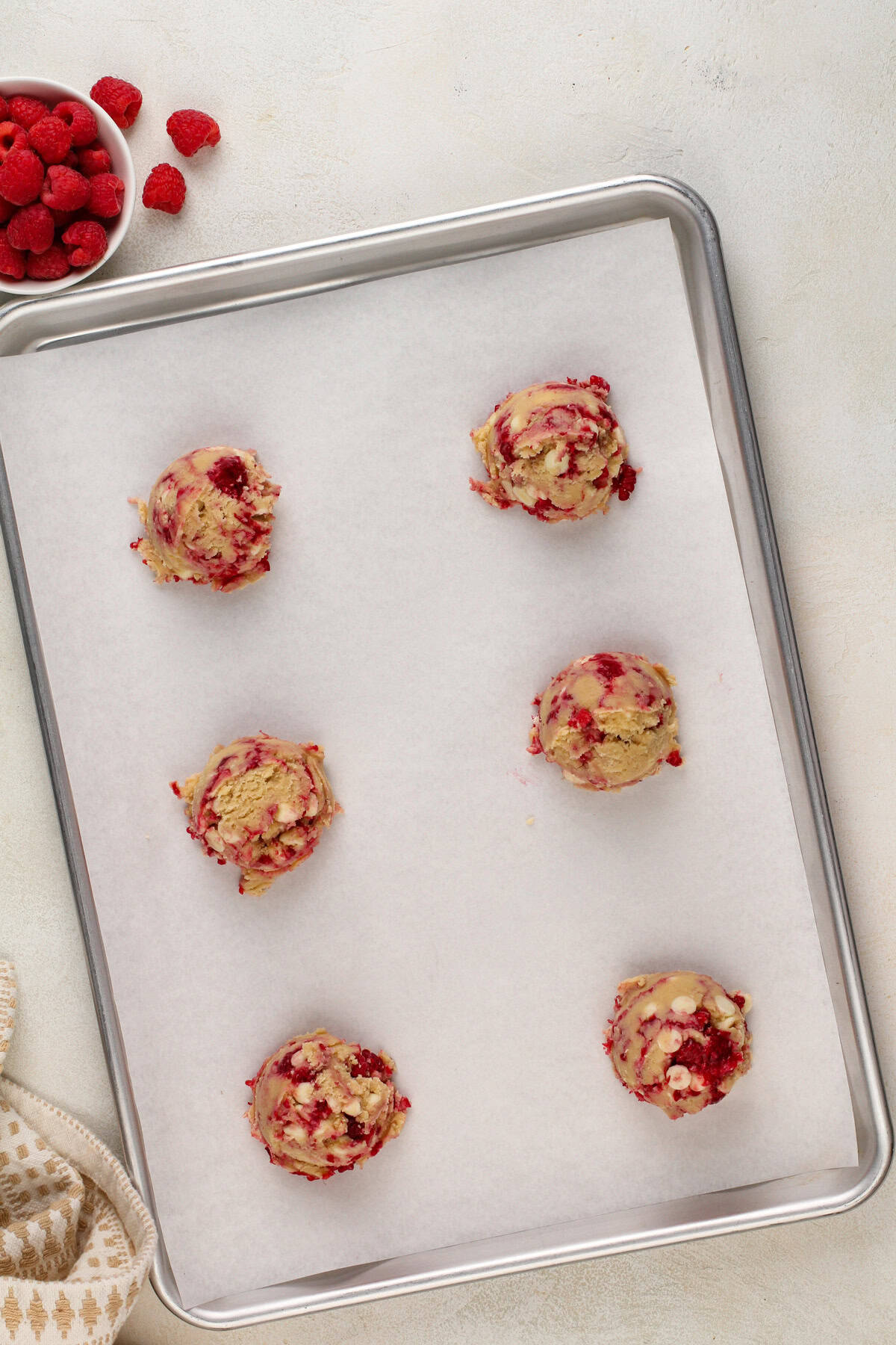 White chocolate raspberry cookie dough portioned on parchment-lined baking sheet, ready to go in the oven.
