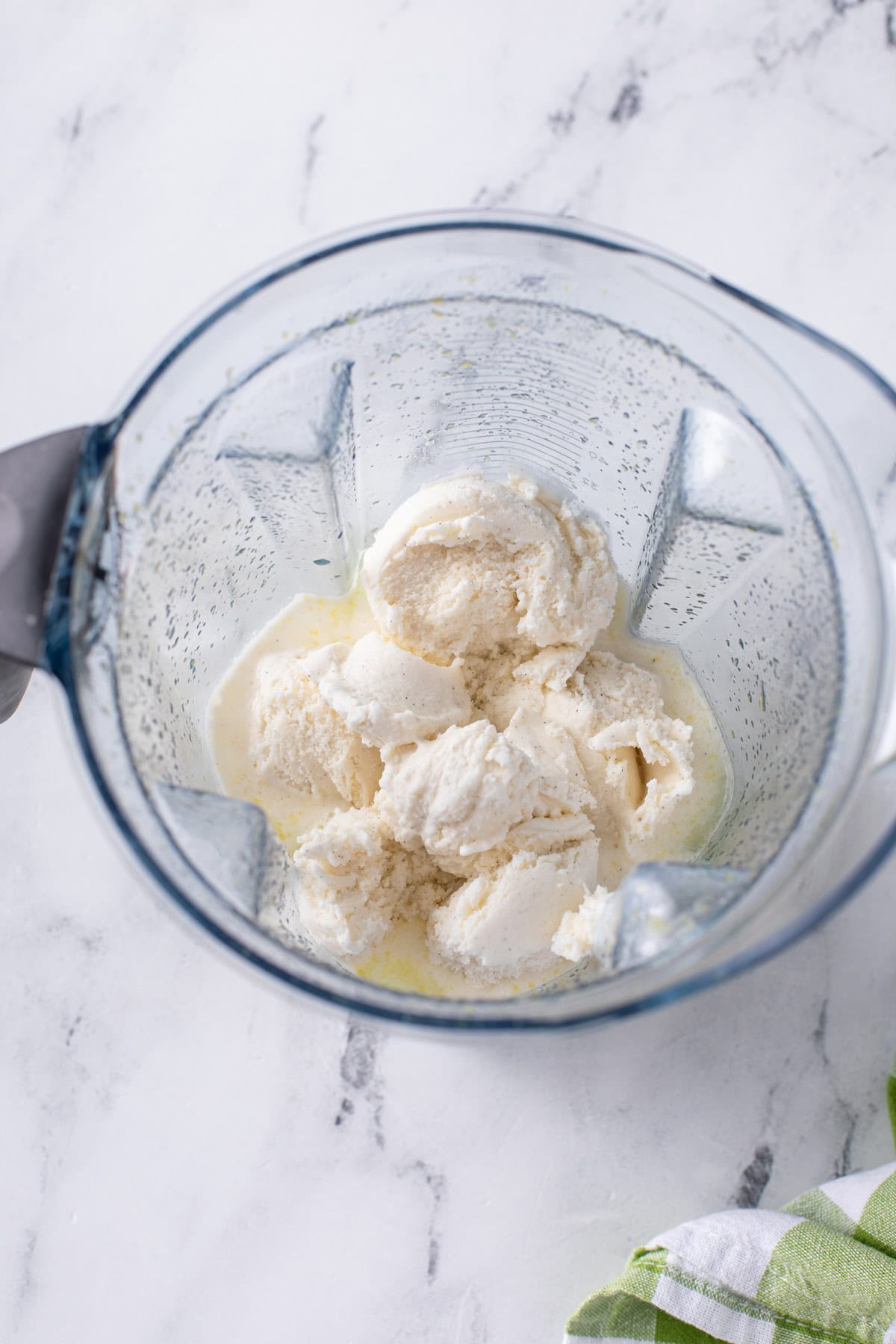 Scoops of vanilla ice cream added to lemon juice, sugar, and water in a blender.