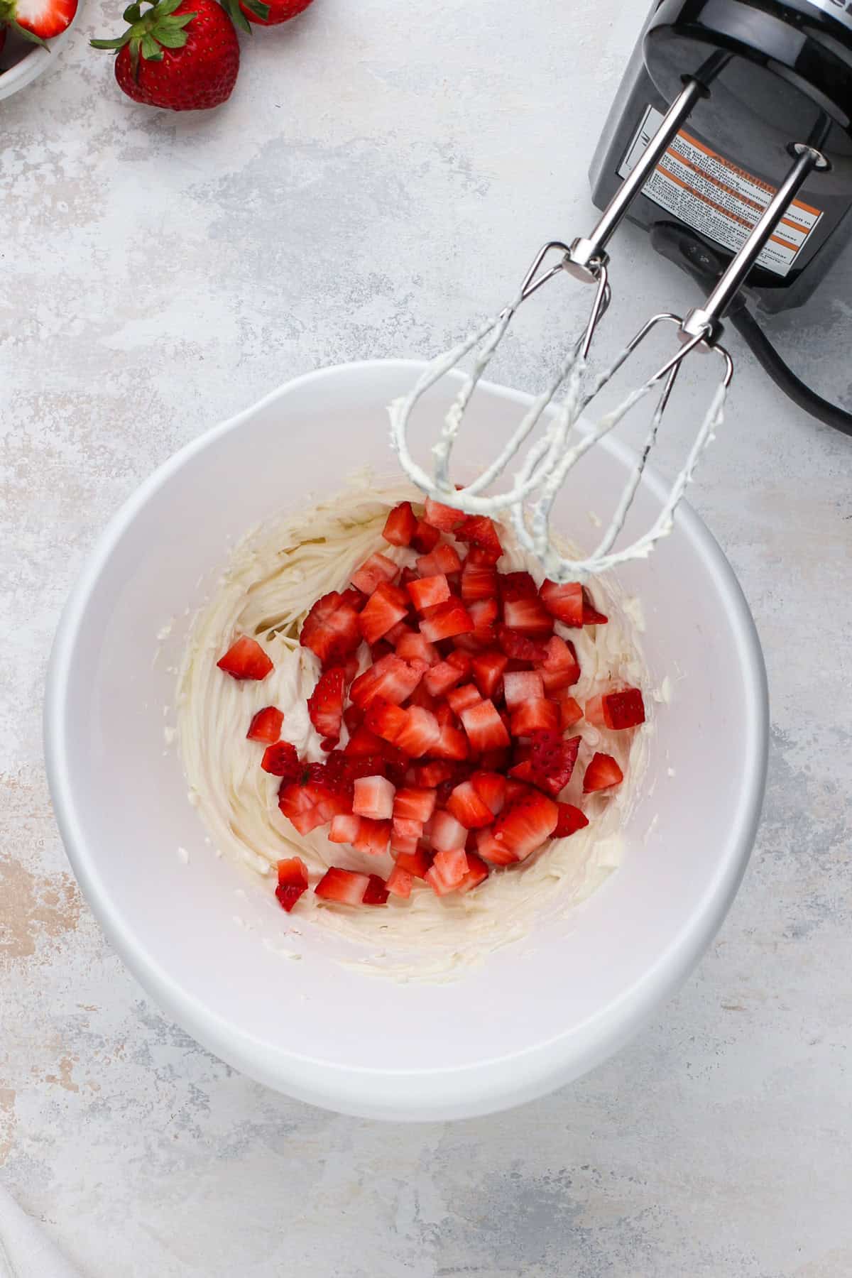 Diced strawberries added to cream cheese in a white bowl.