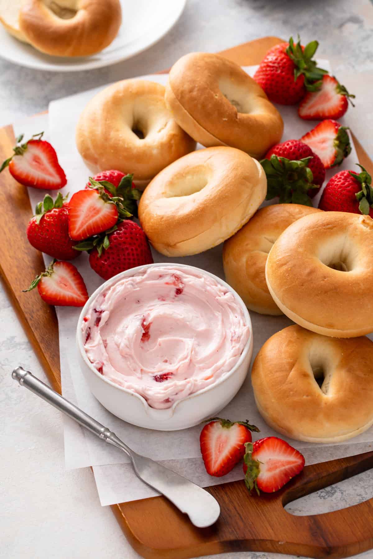 Wooden board filled with bagels, fresh strawberries, and a bowl of strawberry cream cheese.
