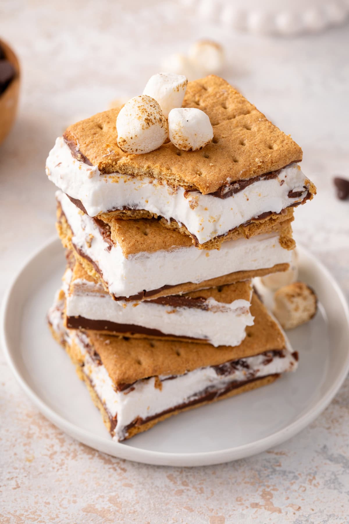 Stack of 4 frozen s'mores on a plate, with a bite taken from the corner of the top s'more.